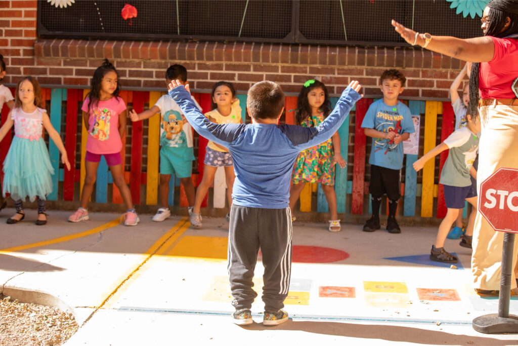 Young boy with arms raised in front of preschool class