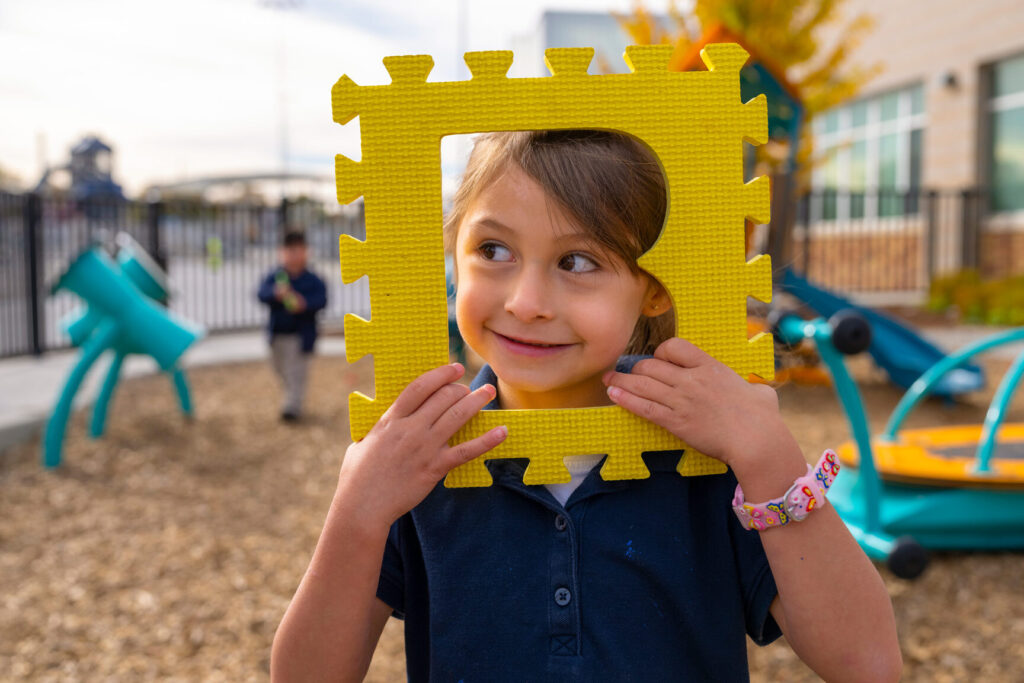 Photo of young girl looking through puzzle piece shaped as a B