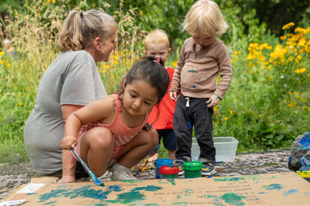 Three preschool children and teacher outside painting