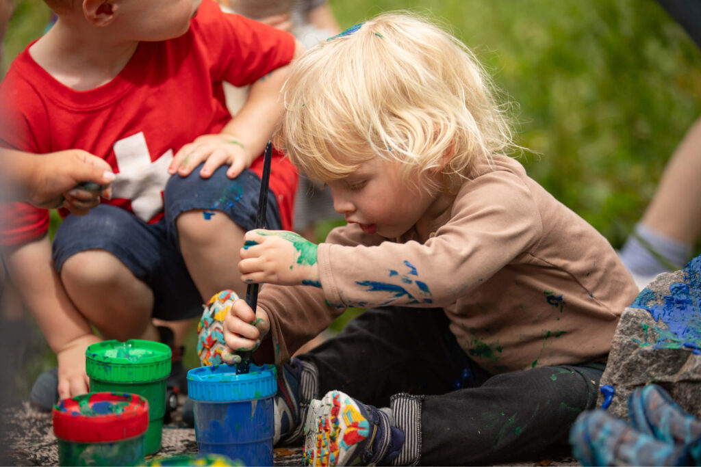 Preschool boy and classmate play with finger paints outdoors