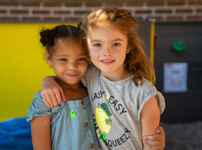 Two preschool girls with arms over one another's shoulders