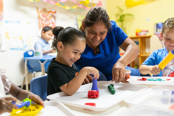 Teacher helping preschool girl with blocks