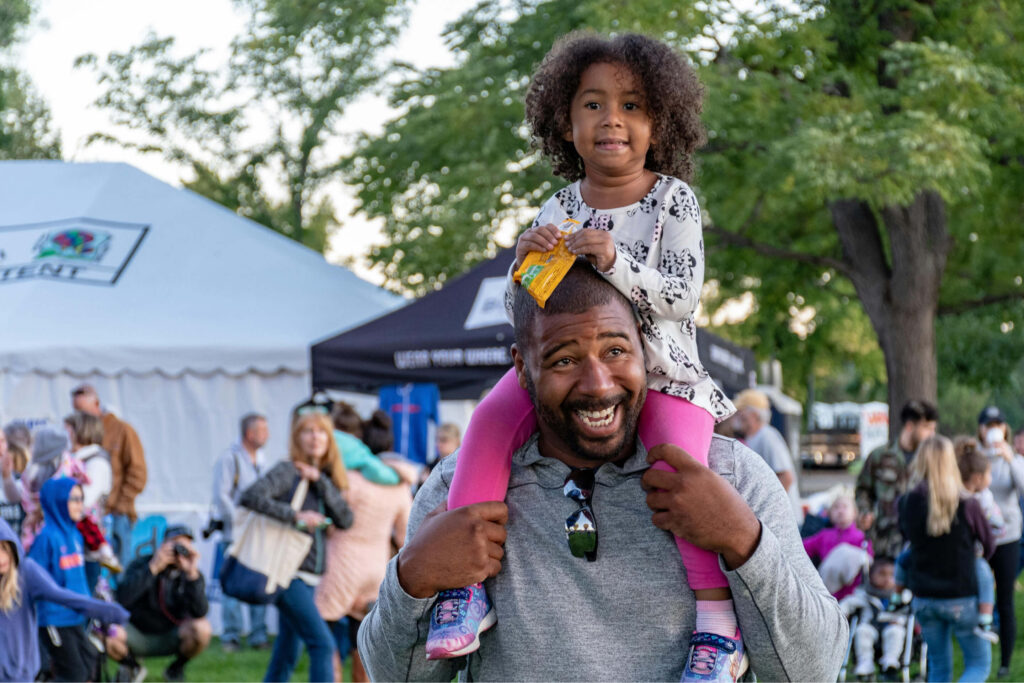 African American father with daughter on his shoulders at a community festival.