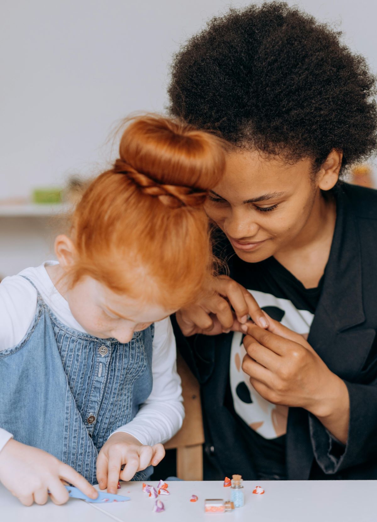 Black female teacher with girl student at table.