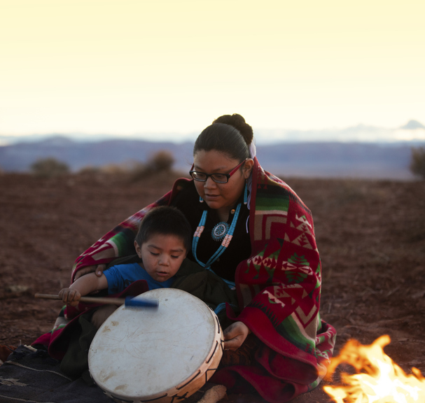 Navajo young woman with child with drum near campfire