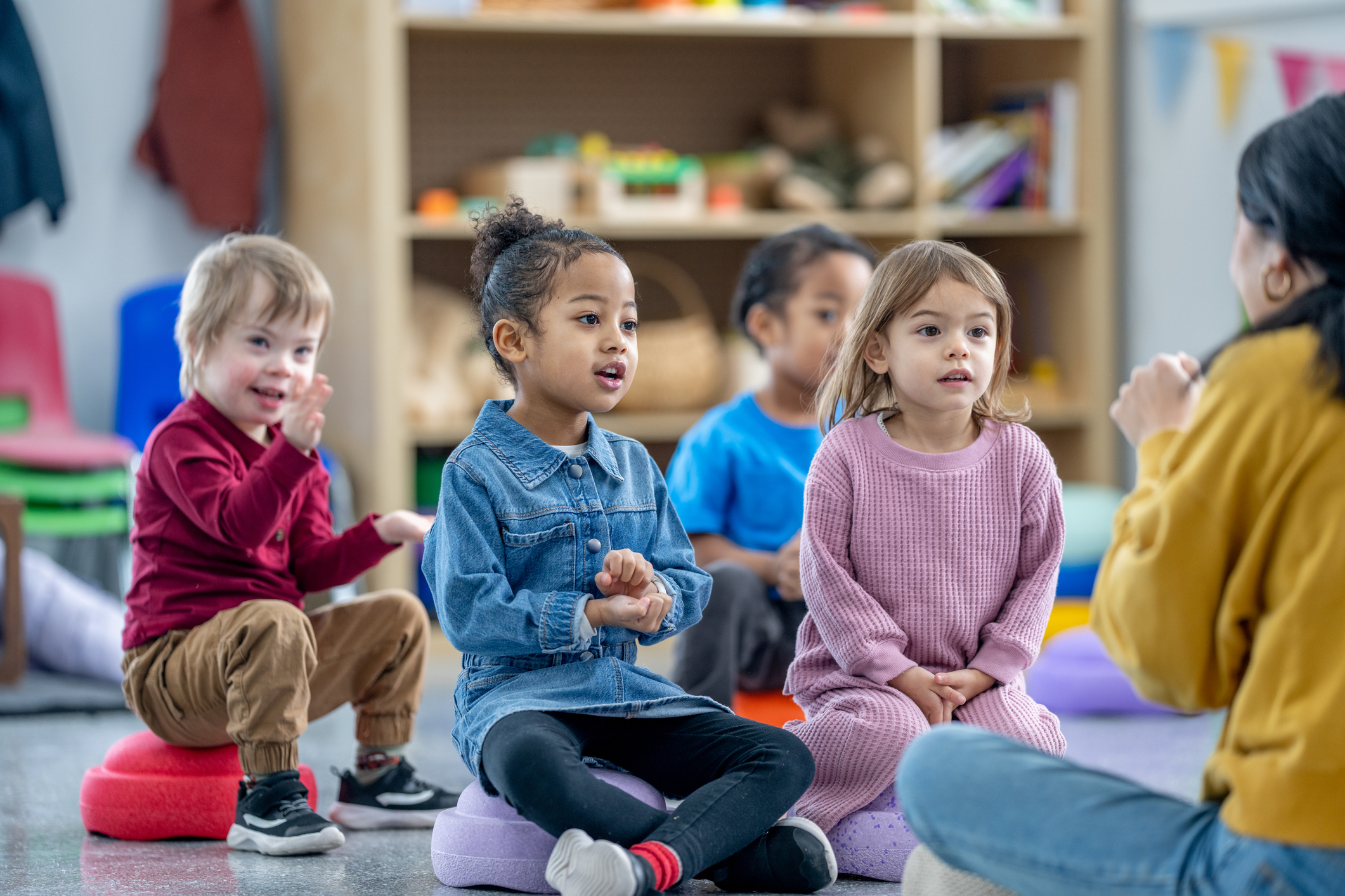 preschool students sitting with teacher for a sing-along.