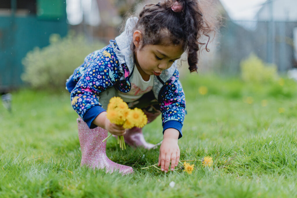 girl with ponytail and rainboots picks flowers