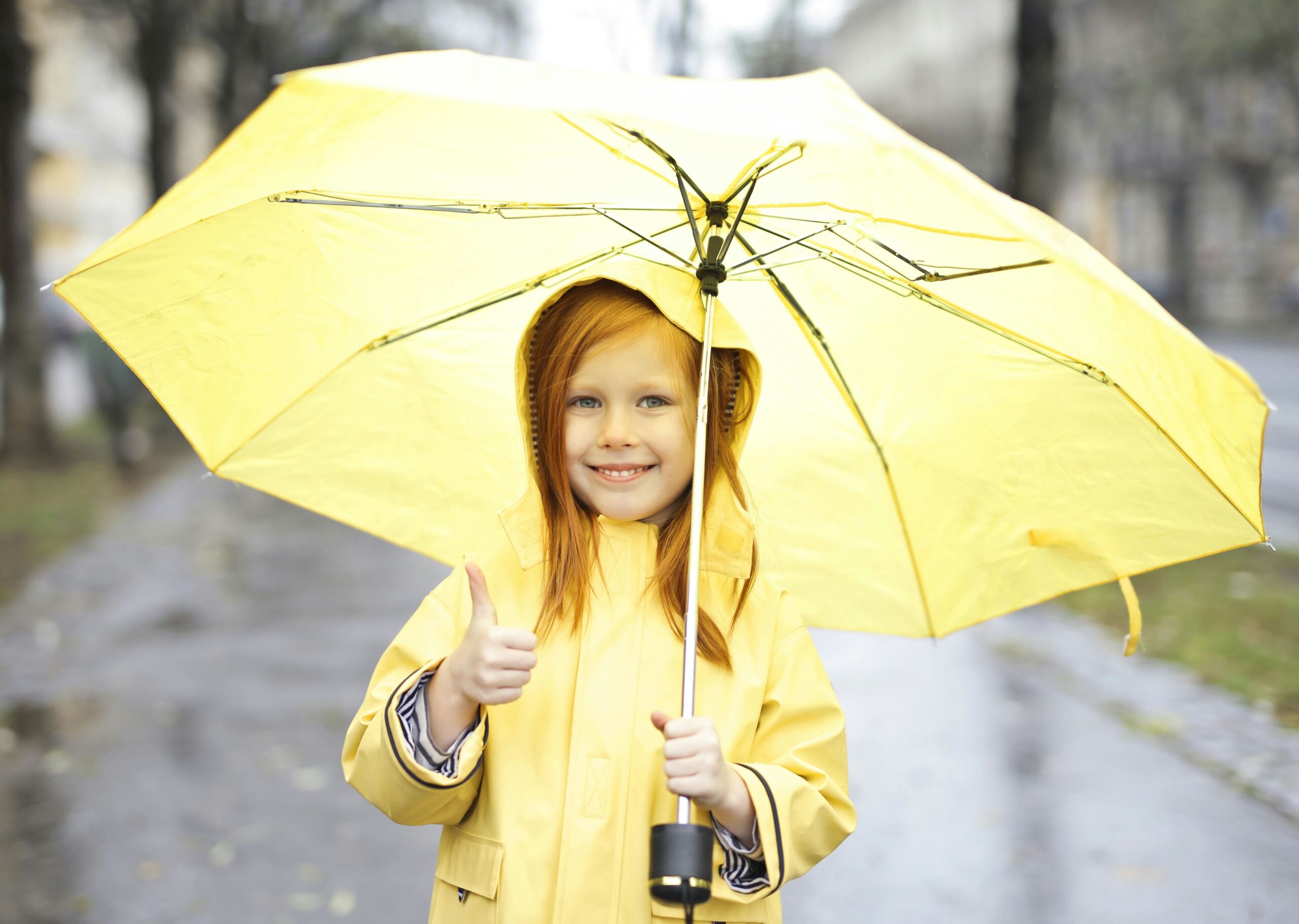 Mädchen in einem gelben Regenmantel mit einem gelben Regenschirm.