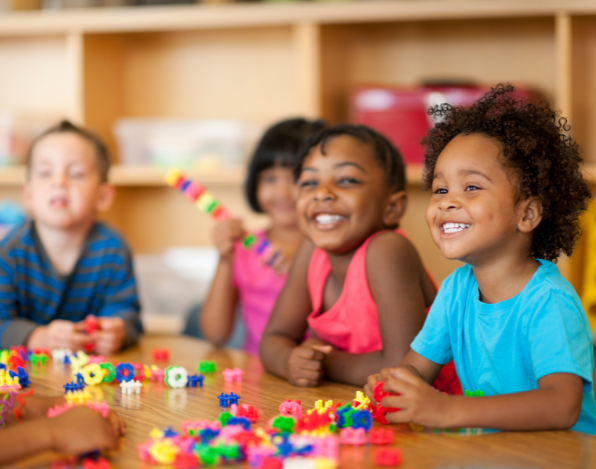 Crianças sorrindo com blocos de brinquedo na frente delas