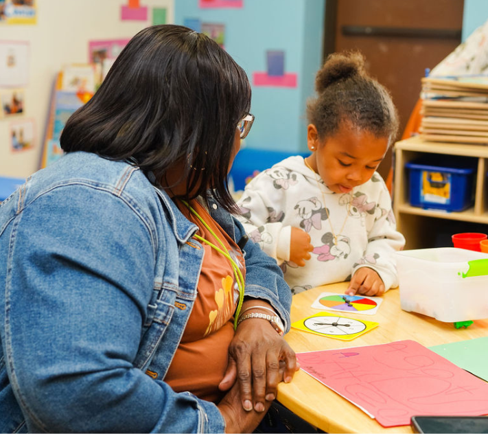 Teacher observing young girl with learning toy