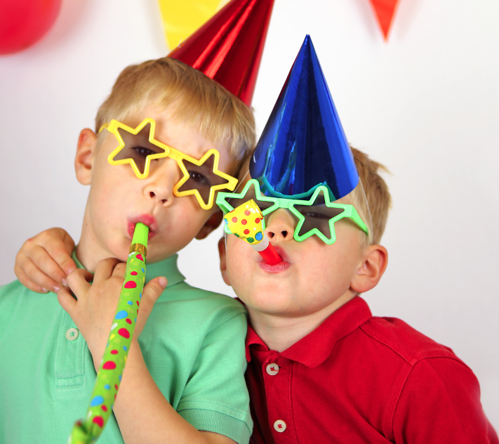 Deux jeunes garçons, coiffés de chapeaux d'anniversaire et portant des lunettes de soleil en forme d'étoile, soufflent dans des instruments de musique.