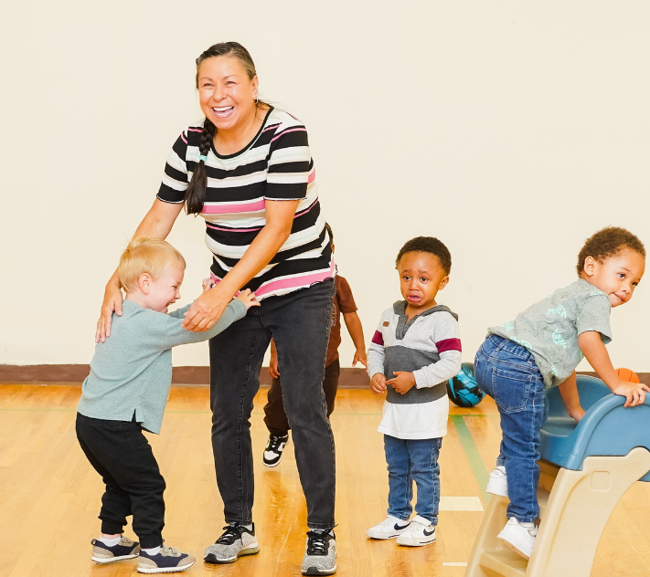 Professora de pré-escola com três meninos brincando ao seu redor.