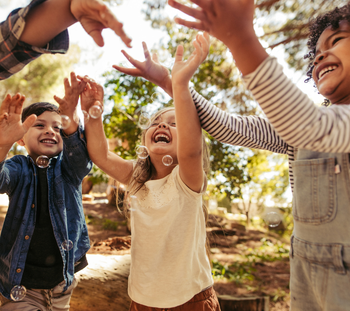 Young children smiling with hands in the air playing with bubbles.