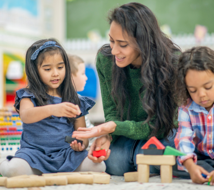 Teacher on the floor with two young preschool children playing with blocks.