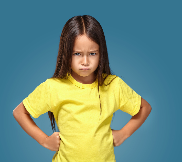 Young girl in yellow shirt scowling with her hands on her hips.